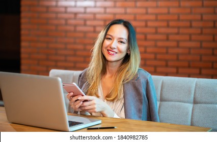 A Korean girl works with pleasure at a laptop and a mobile phone in a loft with brick walls. Modern business running in an urban lifestyle. Work in multitasking mode.