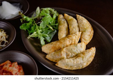 Korean Grilled BBQ combo sets with fried dumplings with salad on the dark plate and black table vibe background, and pickle dishes