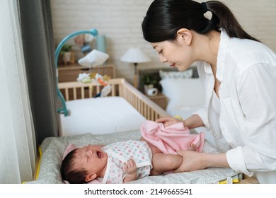 Korean Infant Burst Into Tears Out Of Diaper Rash While Her Mom Is Cleaning Her Bottom. Side View Asian Mother Stays Calm Wiping Her Daughter's Hip While Her Daughter Is Screaming Loudly 