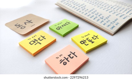 Korean learning for beginner; with focus on many Korean verb written in sticky notes and notebook. Basic verbs vocabulary for Korean language beginner level notes. In white background. 