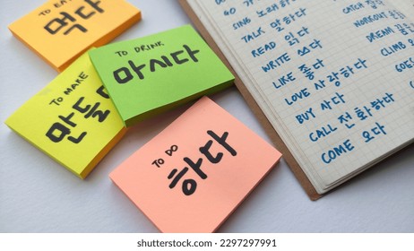 Korean learning for beginner; with focus on many Korean verb written in sticky notes and notebook. Basic verbs vocabulary for Korean language beginner level notes. In white background. 