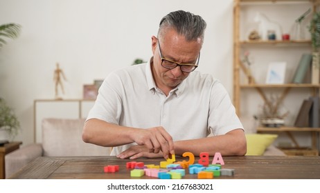 Korean Male Pensioner With Alzheimer’s Disease Trying To Improve Memory By Doing Rehab Exercise For Brain At Home. He Murmurs To Himself While Looking And Counting The Letter Blocks