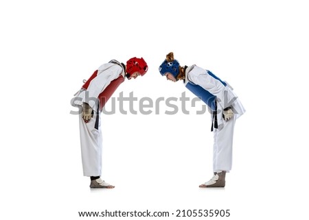 Korean martial arts. Studio shot of two young women, taekwondo athletes greeting each other isolated over dark background. Challenges. Concept of sport, education, skills, workout, health