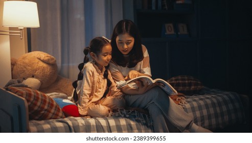 Korean Mother Reading a Fairytale to Her Lovely Small Daughter in Bed Before Going to Sleep. Young Beautiful Mom Caring for Little Girl, Reading Stories from a Book in the Evening at Home - Powered by Shutterstock