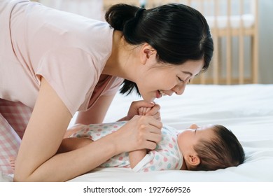 Korean New Mother With Smile Leaning Toward Her Baby Daughter And Holding Her Hands Gently. Portrait Of Mom Having Strong Bonding With Baby.
Mother’s Day Concept
