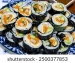 Korean sushi rolls (kimbap or gimbap) cut into small slices and served on a plate. The dish is made from cooked rice and other ingredients rolled up in seaweed sheets or lavers.