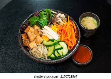 Korean Vegetarian Bibimbap, fried tofu bento box hot stone bowl with salads, kimchi, Bibimbap sauce, miso soup on black table background
