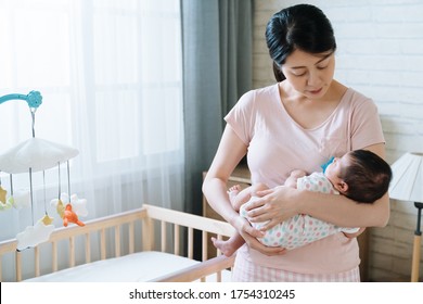 Korean Woman Holding Her Baby Girl Is Walking Her Baby To Sleep In Bedroom. Asian New Mom Watching At Her Child Affectionately While Rocking Her To Bed.