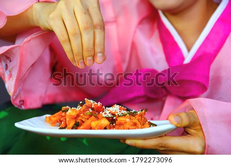 Korean woman in pink National costume show cooking kimchi and the last sprinkled with sesame seeds