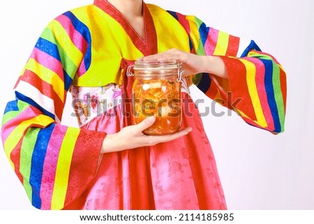 Korean woman wearing hanbok holds a bottle of kimchi With white cabbage, carrot, radish, onion, ginger, apple, chili and salt Is a delicious fermented food