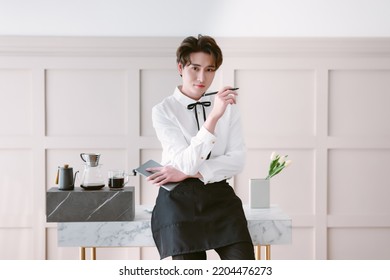 Korean Young Male Barista Entrepreneur Wearing Uniform Holding Digital Tablet And Looking At Camera In Minimal Coffee Shop. Startup Small Business Owner And Sell Online Delivery Business Concept.