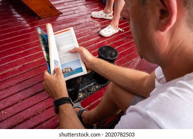 KORNATI, CROATIA - Jul 08, 2021: A Man Reading A Travel Guide During A Boat Excursion 