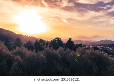 Kos, Greece, Golden sunset over hilly landscape with silhouetted trees and distant mountains under a partly cloudy sky. - Powered by Shutterstock