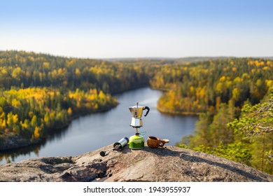 Kouvola, Finland - September 28, 2020: Coffee maker on backpacking stove, wooden cup kuksa and coffee grinder on stone in focus. Background of the forest lake is blurred.