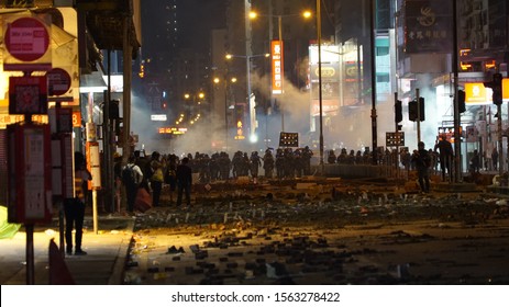 Kowloon, Hong Kong - November 17, 2019: Nathan road in Jordan, covered in bricks during a protest, and rows of riot police with clouds of tear gas in the background. 