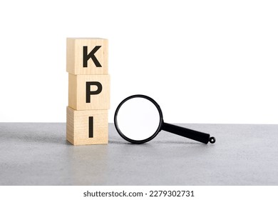 KPI - Key Performance Indicators - text on wooden cubes blocks and magnifying glass on gray table, white background