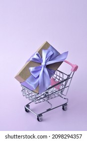 Kraft Gift Box Tied With Purple Ribbon In Shopping Cart. Zero Waste. Eco Friendly, No Plastic. Happy New Year. Very Peri Color. Merry Christmas. 8 March. Birthday. Present. Violet. Shopping. Sale