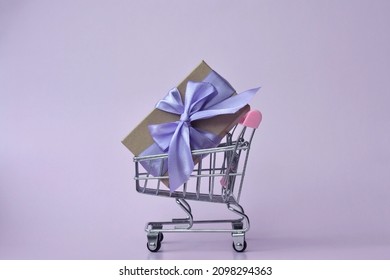 Kraft Gift Box Tied With Purple Ribbon In Shopping Cart. Zero Waste. Eco Friendly, No Plastic. Happy New Year. Very Peri Color. Merry Christmas. 8 March. Birthday. Present. Violet. Shopping. Sale