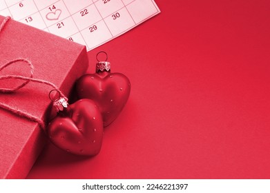 Kraft Gift box with two red hearts and calendar marked February 14, concept of Valentine's, anniversary. Image toned in Viva Magenta, color of the 2023 year.