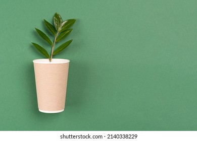 Kraft paper coffee cup with green leaves - biodegradable, compostable paper utensils for hot drinks. Paper cup on green background with copy space. Environmental conservation concept. Selective focus