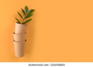 Kraft paper coffee cups with green leaves inside - biodegradable, compostable paper utensils for hot beverages. Paper cup on orange background with copy space. Selective focus