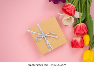 Kraft paper gift box with white ribbon next to vibrant tulips on a pink background. Flat lay arrangement for Mother's Day, spring holidays, and gift-giving concept for card, invitation design - Powered by Shutterstock