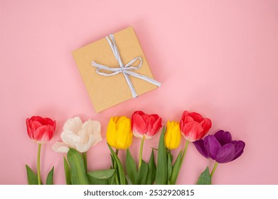 Kraft paper gift box with white ribbon next to vibrant tulips on a pink background. Flat lay arrangement for Mother's Day, spring holidays, and gift-giving concept for card, invitation design - Powered by Shutterstock