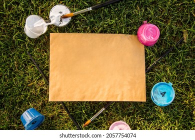 Kraft Paper Rectangular Blank Sheet, Mock Up With Acrylic Color Paint Cans Under Numbers And Paint Brushes On Green Grass. Top View Background. Blank Template