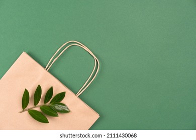 Kraft Paper Recycled Bag With Green Leaves On Green Background With Copy Space. Street Food Take Away Paper Bag, Sustainable Packaging Concept. Ethical Consumerism, Flat Lay