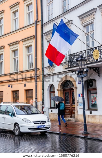 Krakow, poland - APR 30, 2019: France and EU flags\
on facade of Consulate General of the Republic of France in Krakow\
located in historic center of an old town. Citroen car on the wet\
street