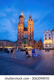 Krakow, Poland - July 23, 2021: A cart with may i help you sign against Saint Maria church at the main square of Cracow, Polish city center at night. UNESCO World Heritage site. Europe