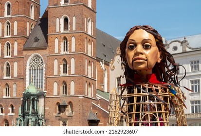 KRAKOW, POLAND - MAY 13, 2022: Little Amal, giant puppet representing Syrian refugee child. Arrives in Kraków to visit Ukrainian war refugees. Saint Mary's Basilica (Mariacki Church) in background.