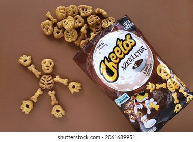 KRAKOW, POLAND - OCTOBER 19, 2021: Bag Of Spilled Puffed Corn Snacks Cheetos Skeleton With Chocolate Flavor On Brown Background. Skeleton Parts: Skull, Rib Cage, Hands, Feets, Bones. Halloween Treats.