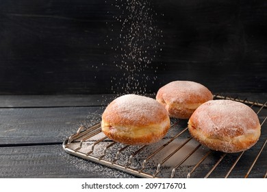 Krapfen or Berliner doughnuts on a baking grid are sprinkled with sugar, fried pastry for New Year or carnival, dark rustic wooden background, copy space, selected focus, narrow depth of field