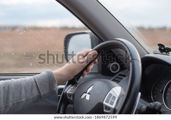 Krasnodar, Russia - 11.02.2020:Male hand on the\
steering wheel of a Mitsubishi car. Autumn rain outside the window.\
Comfortable SUV\
driving