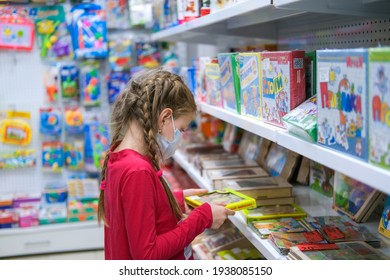 Krasnodar, Russia March 7, 2021. A Child In A Medical Mask Is Choosing A Children's Toy In The Store. A Girl Is Shopping Amid The COVID-19 Pandemic.