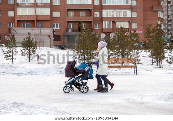 Krasnoyarsk,\
Krasnoyarsk Region, RF - January 8, 2017: Two young mothers are\
walking with strollers along a winter snow-covered street against\
the backdrop of residential\
buildings.