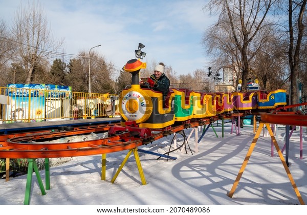 Krasnoyarsk,
Krasnoyarsk Region, RF - March 14, 2021: Children and their
grandmother ride a children's train on high rails over snowdrifts
among trees in a city amusement
park.