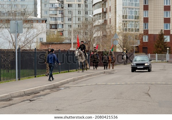 Krasnoyarsk,
Krasnoyarsk Region, RF - May 9, 2021: A group of Cossacks with
flags rides on horseback along the sidewalk against the backdrop of
residential buildings in the spring
city.