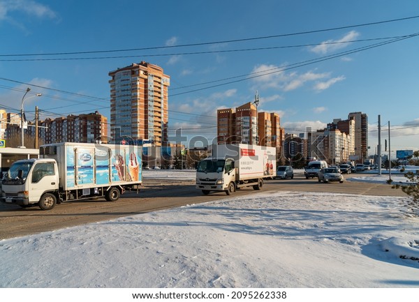 Krasnoyarsk, Krasnoyarsk region, RF - November 26,\
2021: Trucks with refrigerators and other cars drive along a city\
street against the backdrop of residential buildings on a winter\
sunny day.