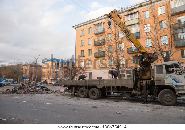 Krasnoyarsk,\
Krasnoyarsk Region / RF - October 29, 2018: Public service workers\
put construction waste from the demolition of old pavilions in a\
truck with a crane on an autumn city\
street.