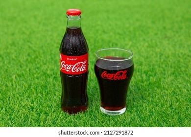 Krasnoyarsk, Russia - 07.14.2020: Glass Bottle Of Coca Cola Covered With Drops Stands On Green Grass Of Lawn. Refreshing Drink. Quenching Thirst. Harm To Health. Unhealthy Food And Drink