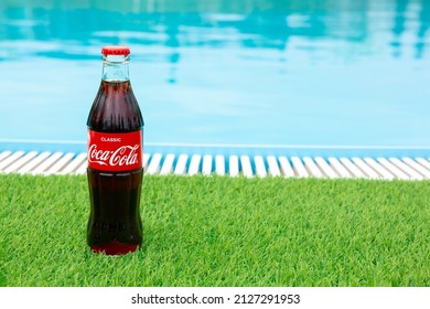 Krasnoyarsk, Russia - 07.14.2020: Glass Bottle Of Coca Cola Stands On Green Grass Of Lawn. Refreshing Drink. Quenching Thirst. Harm To Health. Unhealthy Food And Drink. Place For Text.