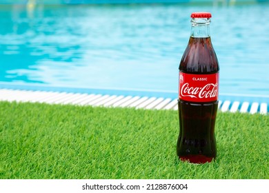 Krasnoyarsk, Russia - 07.14.2020: Glass Bottle Of Coca Cola Stands On Green Grass Of Lawn. Refreshing Drink. Quenching Thirst. Harm To Health. Unhealthy Food And Drink. Place For Text.