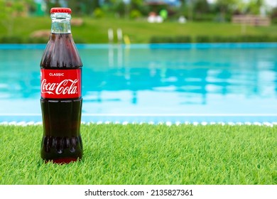 Krasnoyarsk, Russia - 07.14.2020: Glass Bottle Of Coca Cola Stands On Green Grass Of Lawn. Refreshing Drink. Quenching Thirst. Harm To Health. Unhealthy Food And Drink. Place For Text.