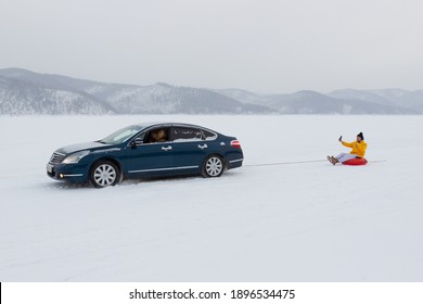 Krasnoyarsk, Russia - 16 January, 2021: A Man Rides A Snow Tube (or Bun, Donut) Tied To A Car On A Snow-covered Lake Surface.