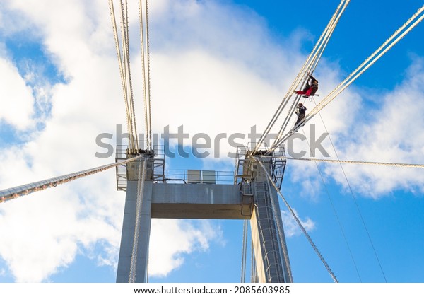 Krasnoyarsk,\
Russia - October 28, 2021: industrial climbers hang on ropes at\
high heights and repair lighting equipment on a cable-stayed\
bridge. Workmen against blue sky\
background.