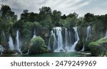 Kravic Falls, Bosnia. Cascades of water flow down into a serene emerald pool, surrounded by lush greenery and trees. It