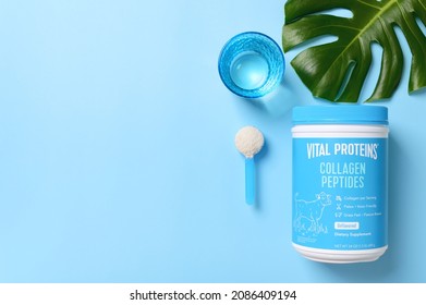 KREMENCHUG, UKRAINE - NOVEMBER 10, 2021: Collagen Peptides Powder Jar With A Measuring Spoon And A Glass Of Water On Blue Background, Top View. Flat Lay With Copy Space. Famous Brand Vital Proteins