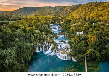 Krka, Croatia - Aerial panoramic view of the beautiful Krka Waterfalls in Krka National Park on a sunny summer morning with green foliage, turquoise water and gold and blue sky at sunrise
